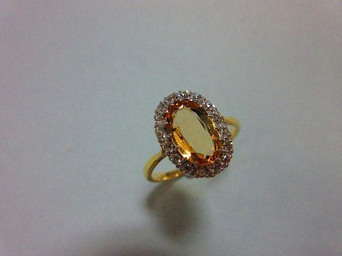 A topaz and diamond cluster ring, the oval cut light orange-brown topaz claw set in a border of sixt