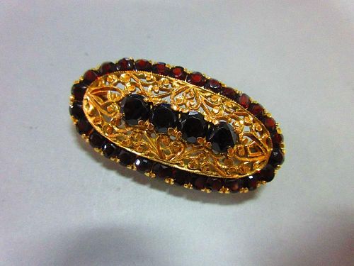 An Italian 18ct gold and garnet brooch, of elongated oval outline delineated by round cut deep red g