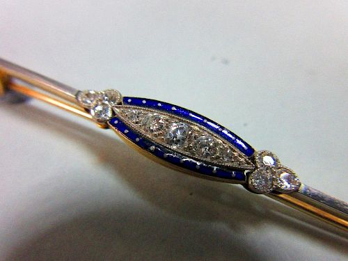 A diamond and enamel bar brooch, set to the centre with a graduated line of five old round brilliant