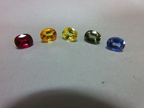 A loose ruby and four loose variously coloured sapphires, all oval to rectangular cushion cut and ev