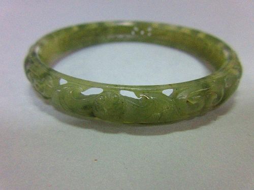 A carved jade bangle, the mottled light green jade of convex profile, pierced and carved with contin