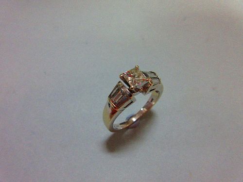 A contemporary princess cut diamond ring, the principal diamond four claw set to flying shoulders ea