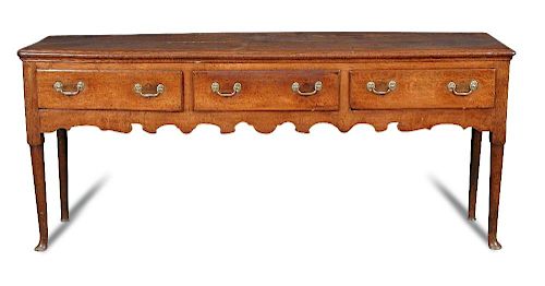 A George III oak dresser base, fitted three drawers with brass handles, shaped fret carved apron on