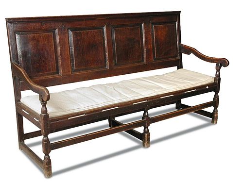 An early 18th century oak panelled settle, with open arms, strung seat and loose cushion, on stretch