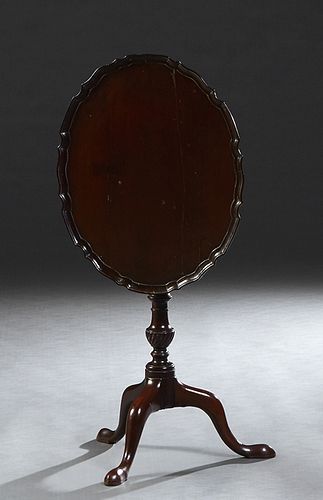 English Carved Mahogany Oval Tilt Top Table, c. 1900, the dished serpentine edge top on an urn form support, to tripodal cabriole legs with pad feet, 