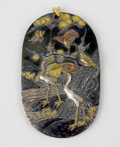 A Japanese shakudo pendant, of oval outline finely decorated with scene of two cranes beside a strea