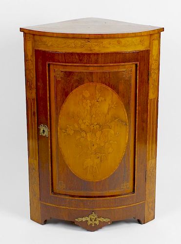 An early 20th century floor standing corner cabinet. The front with curved panelled door, inlaid wit
