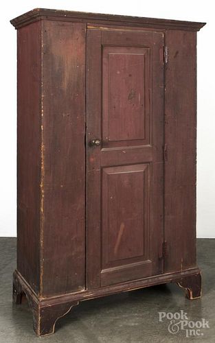 Painted pine wall cupboard, 19th c., with a single raised panel door, retaining an old red surface