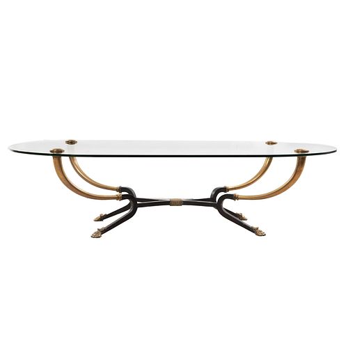 Mesa de centro. SXX. Elaborada en metal dorado y bronce. Cubierta oval de vidrio, chambrana compuesta y soportes tipo garra.