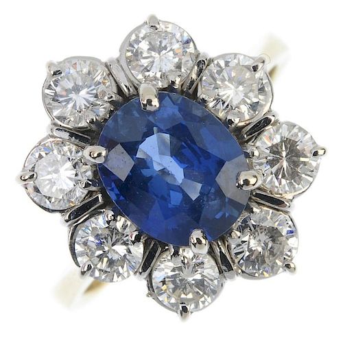 An 18ct gold sapphire and diamond cluster ring. The oval-shape sapphire, within a brilliant-cut diam