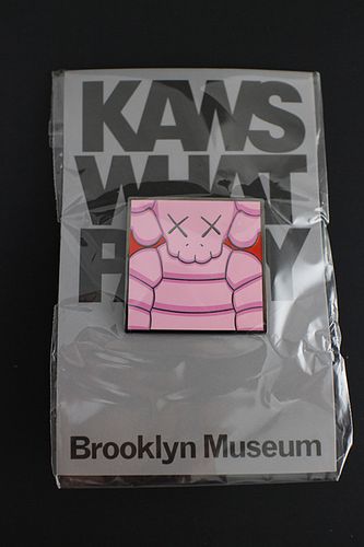 KAWS (American, b.1974) "What Party?" light pink and red square pin, 1 1/2 x 1 1/2 in. Brand new
