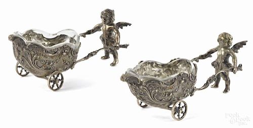 Pair of German 800 silver salt cellars, ca. 1900, in the form of cupid pushing a cart, 5 3/4'' l.