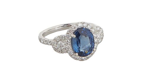 Lady's Platinum Dinner Ring, with an oval 3.42 carat blue sapphire atop a border of small round diamonds, with diamond mounted lugs and shoulders of t