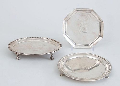 TWO GEORGE III SILVER TEAPOT STANDS AND A GEORGE III CRESTED OCTAGONAL SMALL TRAY