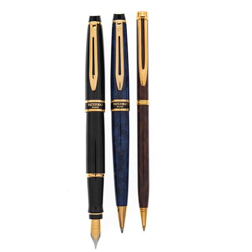 Artículos de escritura pluma fuente y dos bolígrafos de la firma Waterman. Cuerpos en acero en color negro, tabaco y azul acabado...