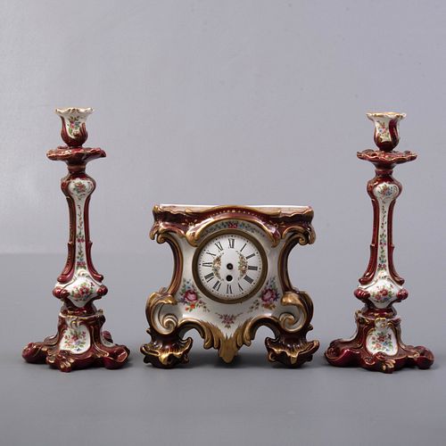 Guarnición. Italia, SXX. Elaborada en porcelana. Capodimonte. Consta de: reloj de mesa y par de candeleros.