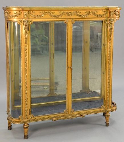 Louis XVI style gilt vitrine having onyx top on cabinet with bowed glass sides, glass shelves, and mirror back, all set on tu