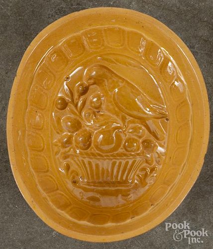 Yellowware food mold with a parrot perched on a basket of fruit, 3 1/4'' h., 8'' w., 7'' d.
