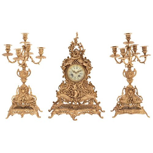 GUARNICIÓN. EUROPA, SIGLO XX. Fundición en bronce y metal dorado. Consta de: reloj y par de candelabros. Reloj con mecanismo de cuerda.