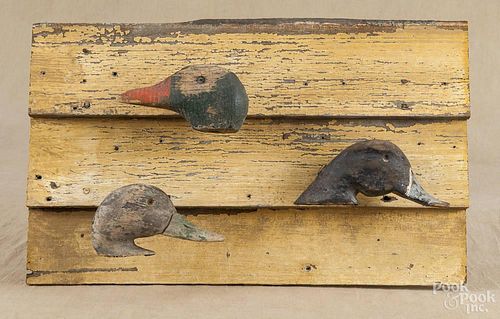 Three carved and painted duck decoy heads, 20th c., mounted to a piece of painted clapboard siding