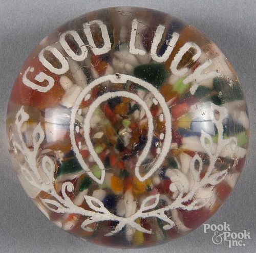 White frit paperweight, with a horseshoe, inscribed Good Luck over a multicolored chip ground, 2 3