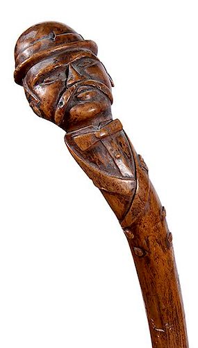 319. Folk-Art Man Cane – Ca. 1880 – A carved one-piece burl with a gentleman atop in a boiler hat/handlebar mustache, bow