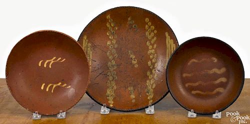 Three Pennsylvania redware plates, 19th c., with slip decoration, 7'' dia., 7 3/4'' dia., and 10 1/4