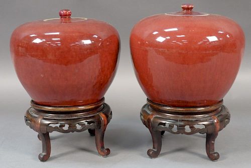 Pair of San de Boeuf ginger jars, oxblood red glazed jars with porcelain covers on stands. 
ht. 7 1/2in., dia. 9in.