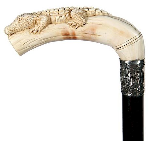 69. Alligator Dress Cane- 20th Century- A carved “pig ivory” gator, ornate silver metal collar, ebony shaft and a metal f
