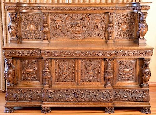Oak sideboard having carved panel back with compote of fruit supported by winged griffins set on cabinet having three carved