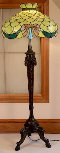 Carved wood floor lamp having carved ram's heads slender shaft and three downswept members with hoof feet, having leaded glas