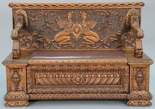 Victorian carved oak bench with curved panel back and leather lift seat, carved face arm supports and carved front and face c