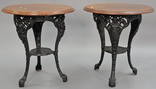 Pair of oak top cafe tables with iron base having female figures and paw feet, ht. 28in., dia. 26in. Provenance: Property fro