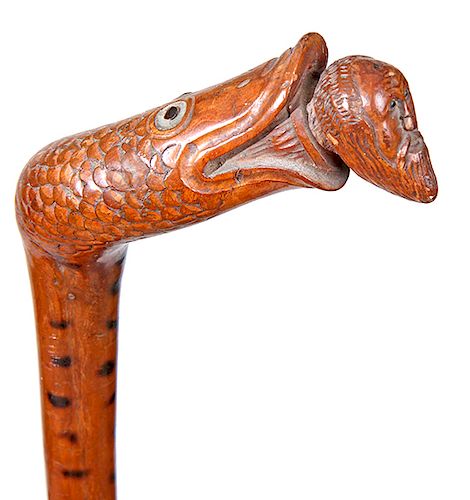 121. Folk-Art Jonah Cane- Ca. 1880- A whimsical carving of a giant fish with pearl and glass beaded eyes swallowing Jonah with glass eyes and a long b