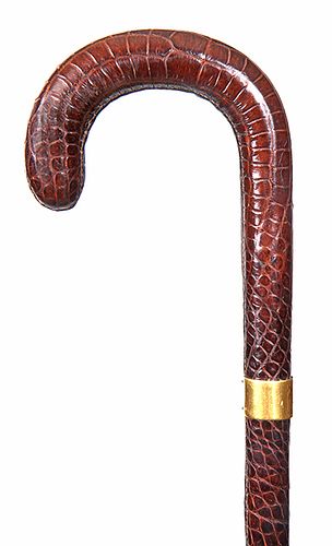 124. A  Crocodile Dress Cane- Mid 20th Century- A fully covered crook handle with tanned skin, 18 karat gold signed collar and a black horn ferrule. H