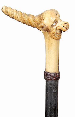 189. Whimsical Stag Cane- Ca. 1890- A carved antler with a whimsical carving with a gentlemen with a long nose and two color glass eyes, braided leath