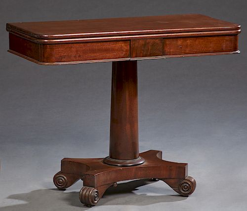 American Classical Carved Mahogany Games Table, 19th c. the rounded corner top swiveling to open storage, on a tapering cylindrical support to a quadr