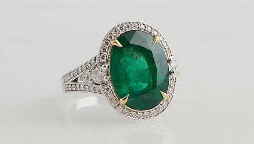 Lady's 18K White Gold Dinner Ring, with an oval 9.25 carat emerald atop a border of round diamonds, the tapered pierced shoulders with central graduat