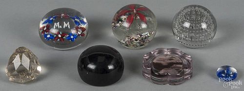 Seven assorted glass paperweights of varying sizes.