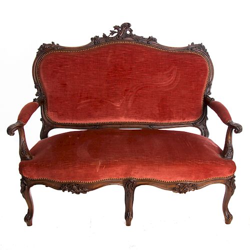 Love seat. Francia. Siglo XX. Estilo Luis XV. En talla de madera de nogal. Con tapicería de tela color rojo.