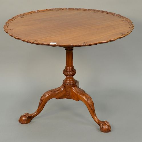 Margolis mahogany piecrust tip table with carved top, 
on fluted and carved shaft, set on tripod base ending in ball and claw feet. ...