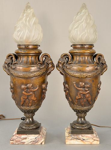 Pair of bronze torchiere form figural table lamps, 
frosted flame form shades over bronze urn body with rams head handles and molded...