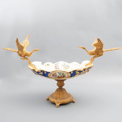 Centro de mesa. Siglo XX. Elaborado en porcelana. Con soporte y aplicaciones de metal dorado. Decorado con esmalte dorado.