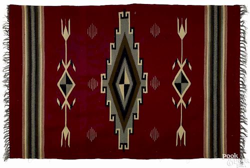 Navajo weaving with stylized geometric designs on a red field, 72'' x 47''.