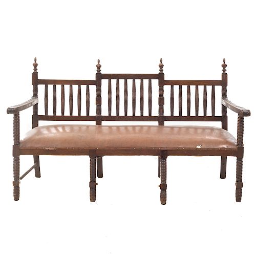 Banca. Siglo XX. En talla de madera. Con respaldo semiabierto, asiento acojinado de piel color marrón. Dimensiones: 100 x 162 x 67 cm.