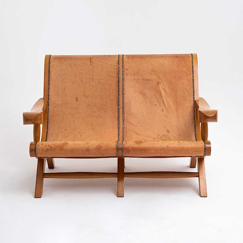 Love seat. México, siglo XX. Estilo Miguelito. Elaborado en madera. Diseño curvo. Con respaldo y asiento en tapicería de cuero café.