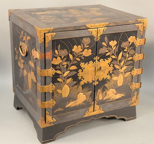 Japanese black lacquered cabinet, having heavy paint gilt landscape with blossoming flowers and leaves, two doors opening to reveal seven drawers of v