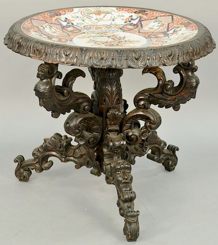 Carved Walnut Center Table, inset Imari porcelain dished top on carved base with carved figural masks. height 29 1/2 inches, diameter 33 inches.