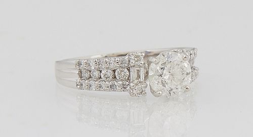 Lady's Platinum Dinner Ring, with a central 1.15 carat round diamond atop baguette diamond mounted lugs, the tapering shoulders of t...