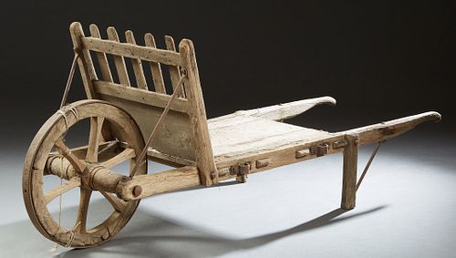 French Provincial Carved Pine Primitive Wheelbarrow, 19th c., with a spiked iron rimmed wheel on one end and two handles on the othe...